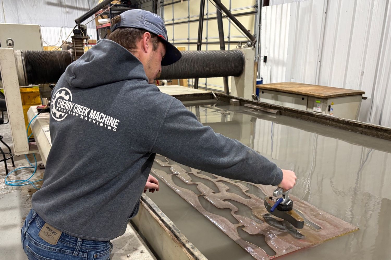 Cherry Creek Machine machinist removing waterjet-cut steel parts from a nested plate on the OMAX 80X in Tulsa, Oklahoma